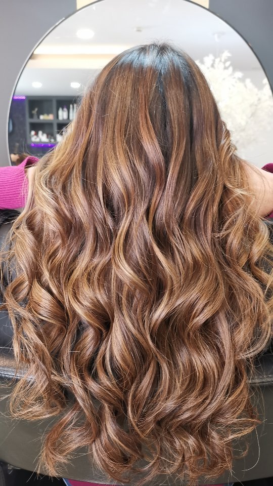 Cabelo castanho com reflexos quentes e acabamento ondulado, visto de costas.