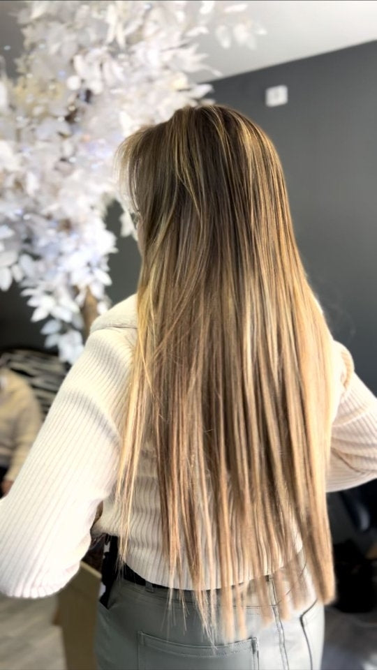 Cabelo comprido com acabamento liso, raiz mais escura e reflexos claros.